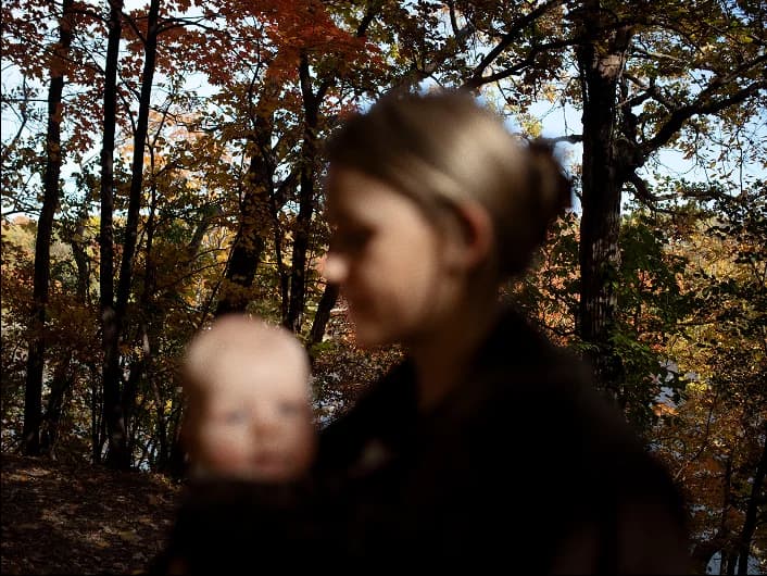 A parent carrying a baby through autumn woods